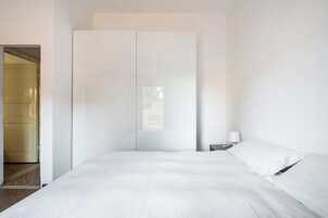 Camera da letto minimalista con un letto grande, un armadio e un comodino con una lampada.