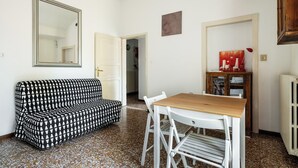 Una habitación con un sofá estampado, una mesa de madera con sillas, un espejo y un radiador.