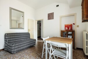 Una stanza con un divano decorato, un tavolo di legno con sedie, uno specchio e un termosifone.