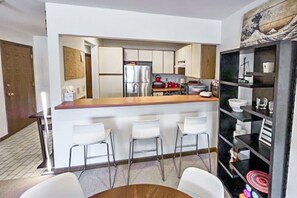 A modern kitchen with a central island, bar stools, and a black shelving unit with various items.