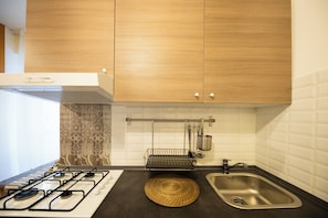 A modern kitchen with wooden cabinets, a gas stove, a sink, and a hanging pot rack.