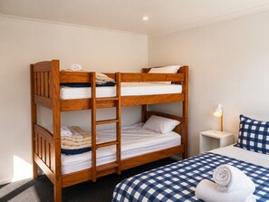 A bunk bed with three levels, a bedside table with a lamp, and a checkered bedspread.