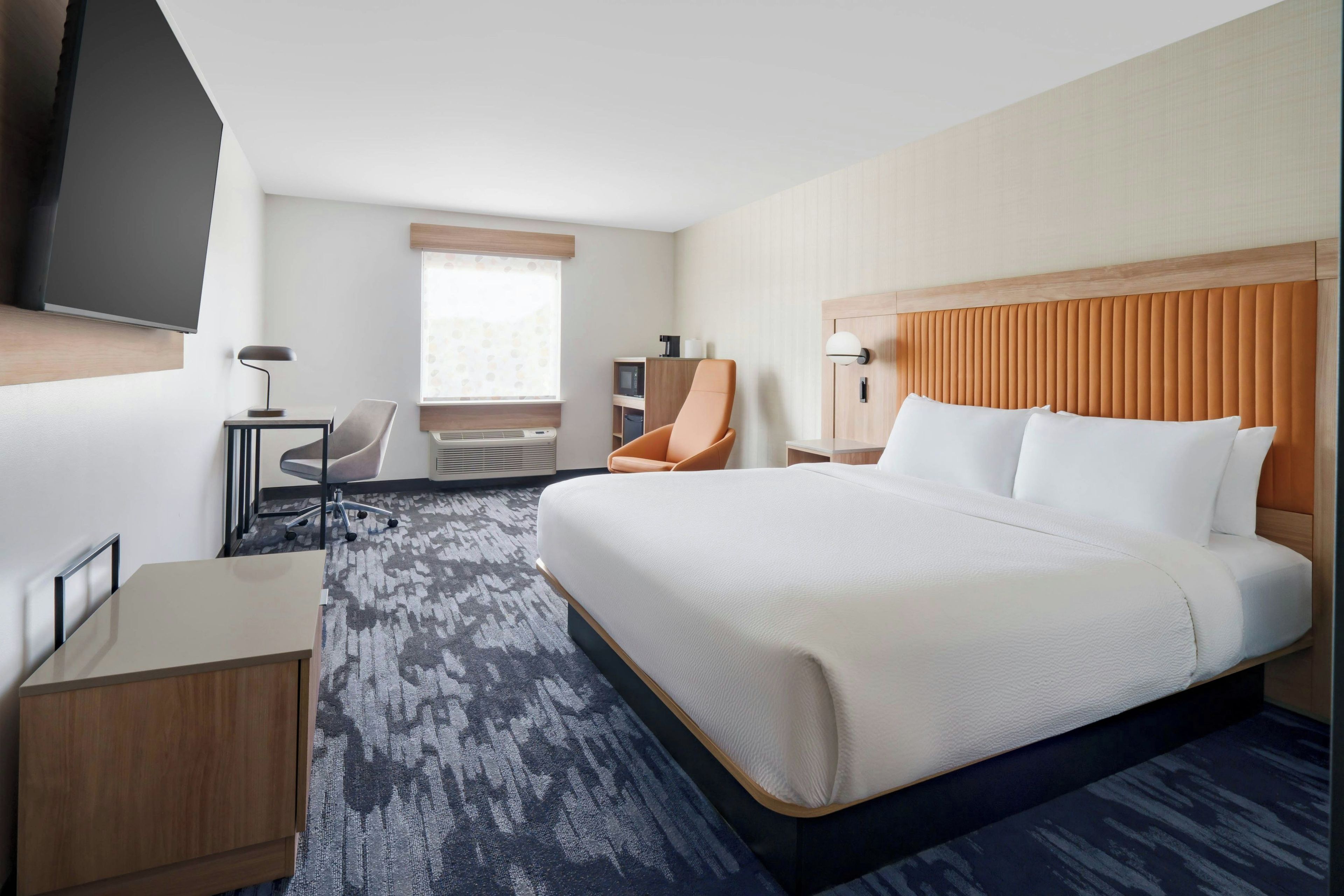 A hotel room with a large bed, a desk, a chair, a television, and a window with blinds.