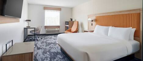A hotel room with a large bed, a desk, a chair, a television, and a window with blinds.