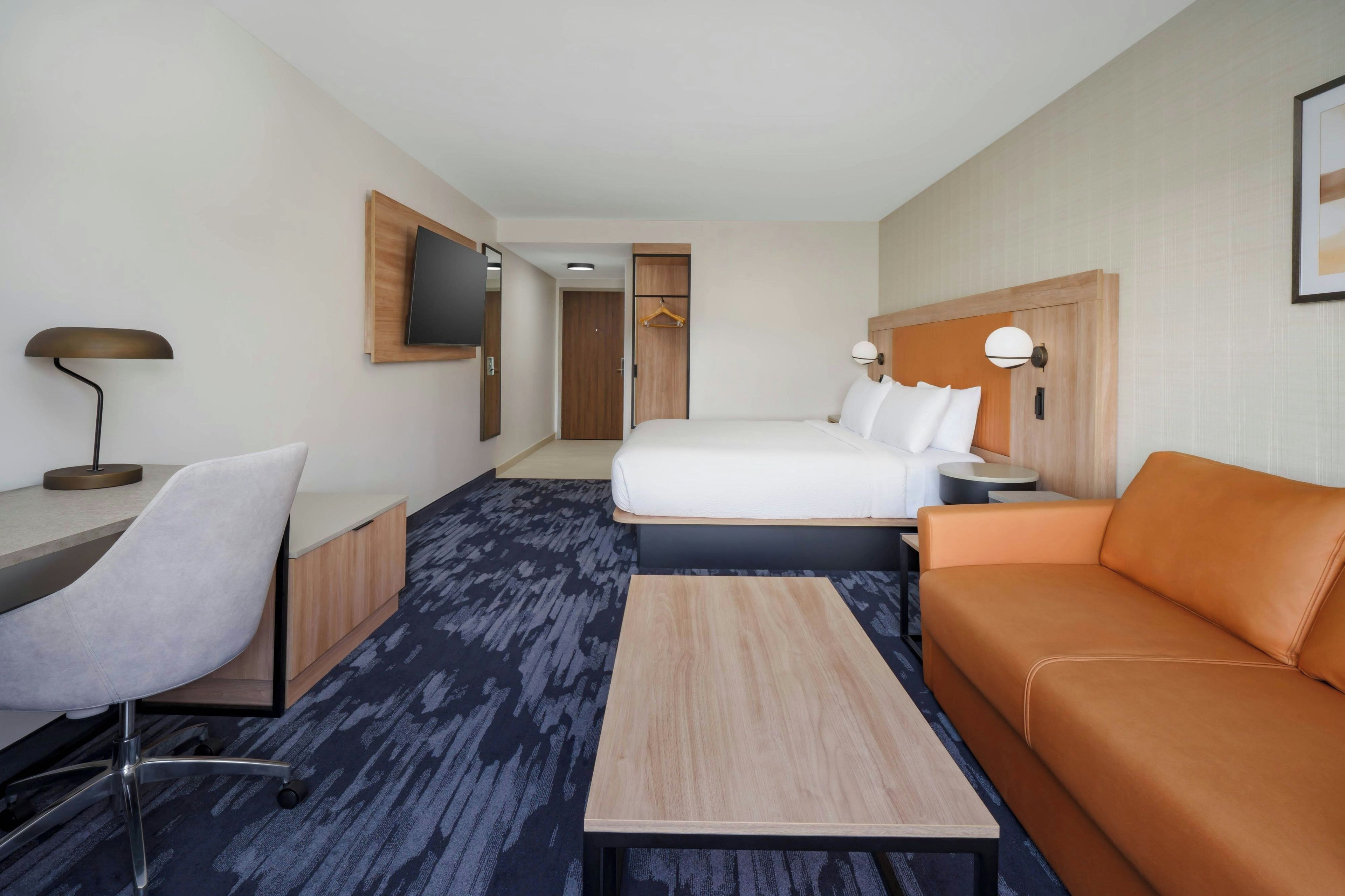 Habitación de hotel con cama, escritorio, silla, sofá, televisor y armario.