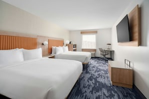 A hotel room with two beds, a desk, a chair, a television, and a window with a view.