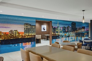 Un espace de restauration moderne agrémenté d’une fresque représentant un paysage urbain, de panneaux en bois et de mobilier contemporain.
