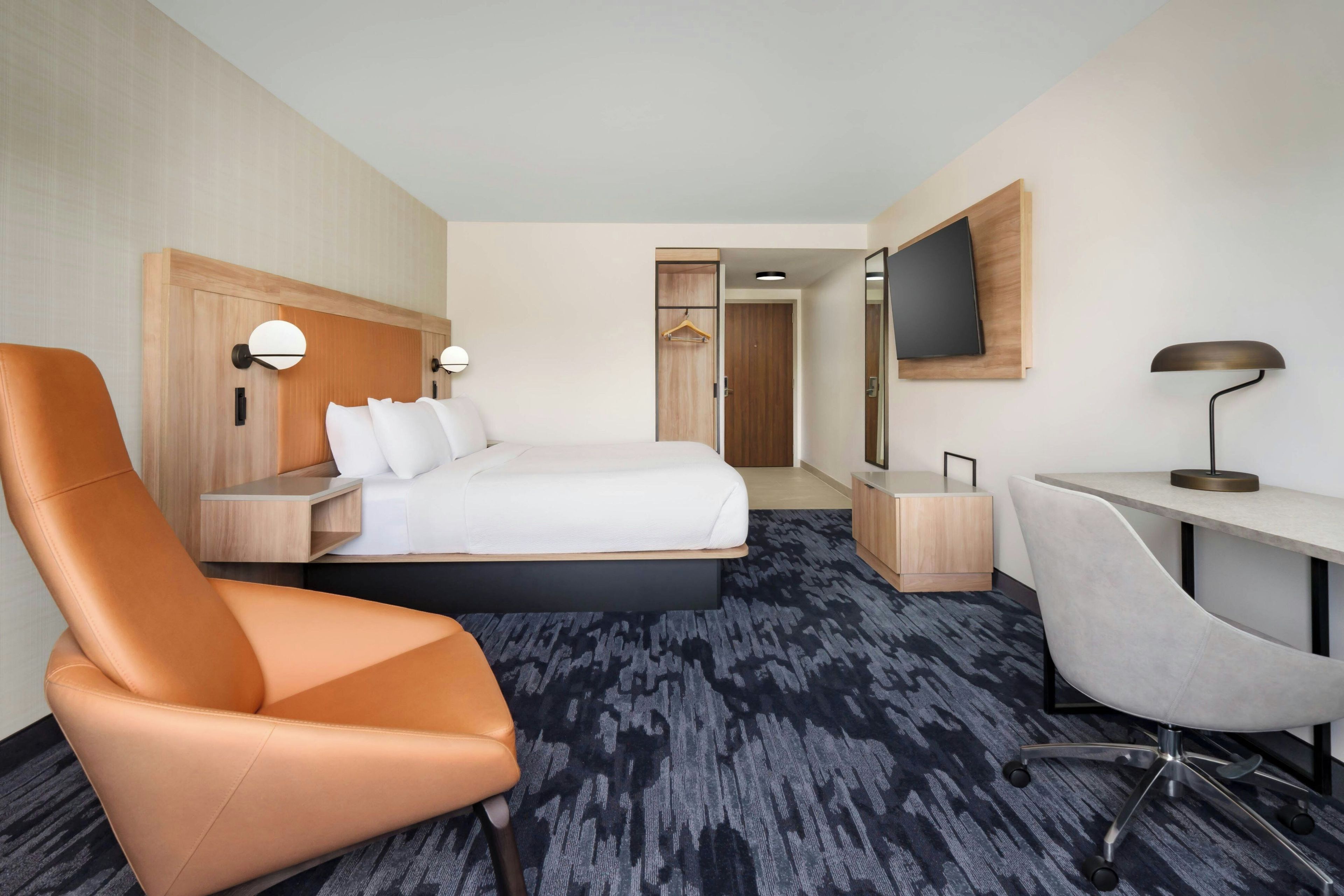 Una habitación de hotel con cama, escritorio, silla, televisión y armario.