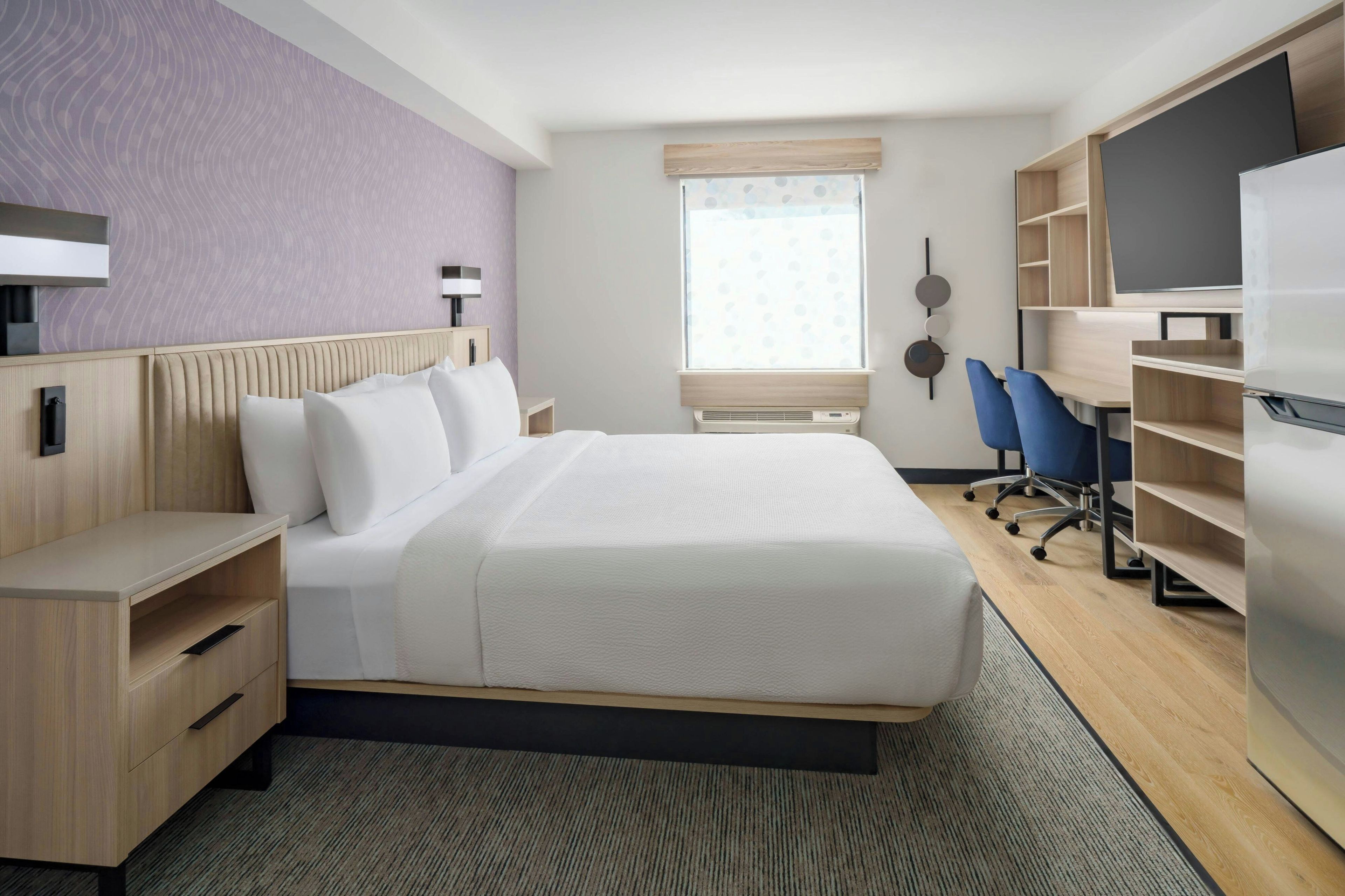 Una habitación de hotel moderna con una cama grande, un escritorio, una silla, un televisor y una ventana con persianas.