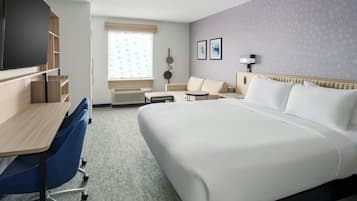 A hotel room with a large bed, a desk with a chair, a sofa, a small table, and a TV.