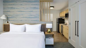A hotel room with a bed, bedside lamp, a view of the kitchen, and a wall with a blue abstract design. - Towneplace Suites By Marriott East Hartford (East Hartford)