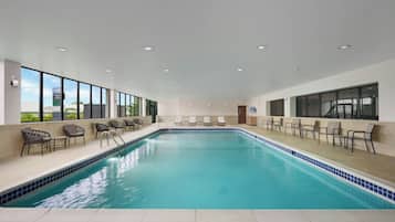 A large indoor swimming pool with clear blue water, surrounded by lounge chairs and a tiled deck.
