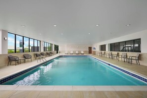 Une grande piscine intérieure à l’eau d’un bleu cristallin, entourée de chaises longues et bordée d’une terrasse carrelée.