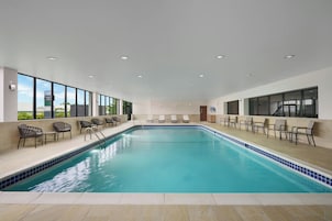 Una amplia piscina interior con agua cristalina, rodeada de sillas de descanso y un solárium con baldosas.