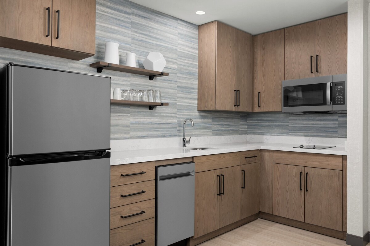 A modern kitchen with wooden cabinets, a stainless steel refrigerator, a microwave, and a dishwasher.