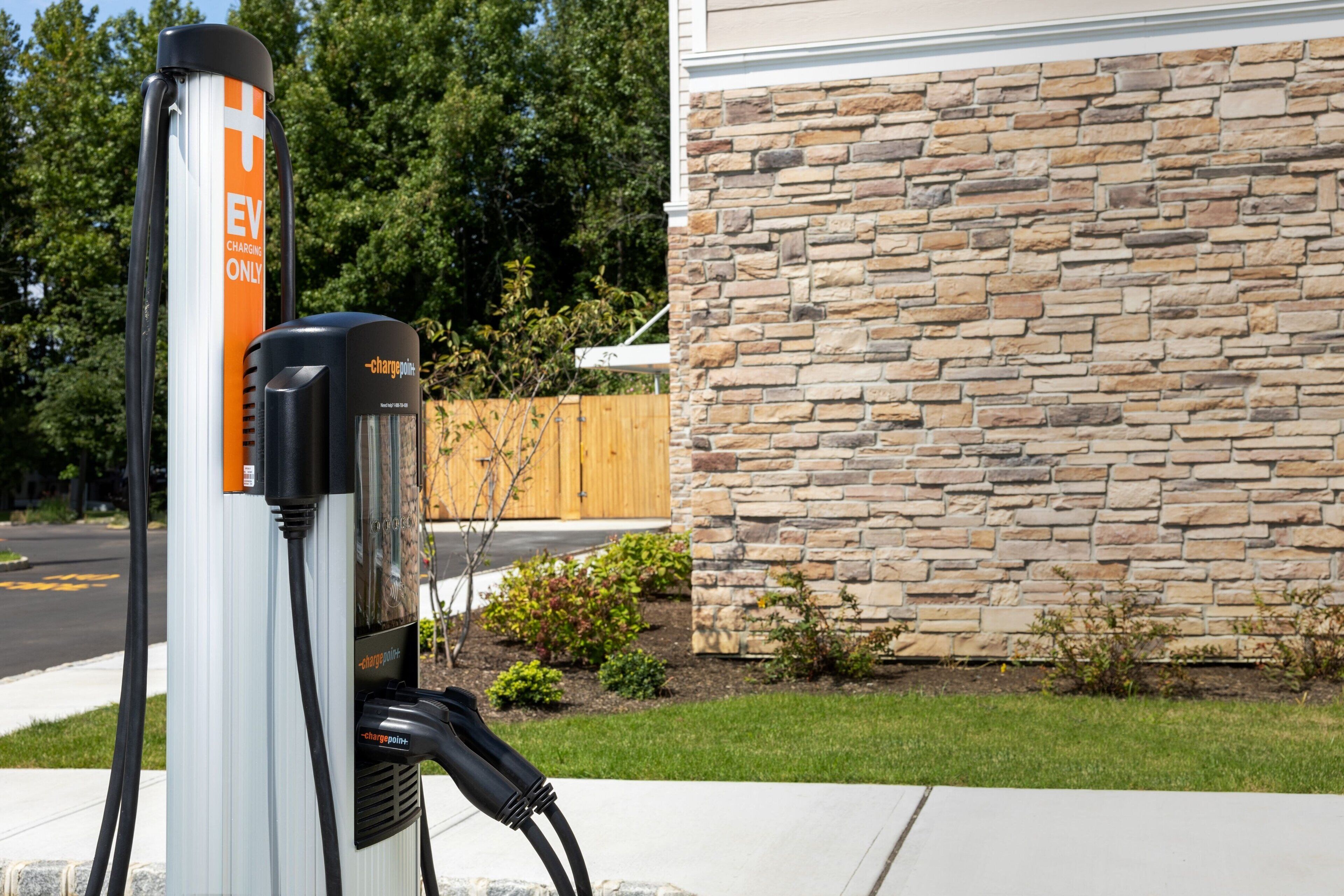 An electric vehicle charging station with a stone wall and a wooden fence in the background.
