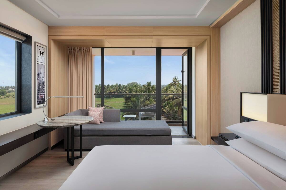A modern hotel room with a large window, a sofa, a bed, and a small table.