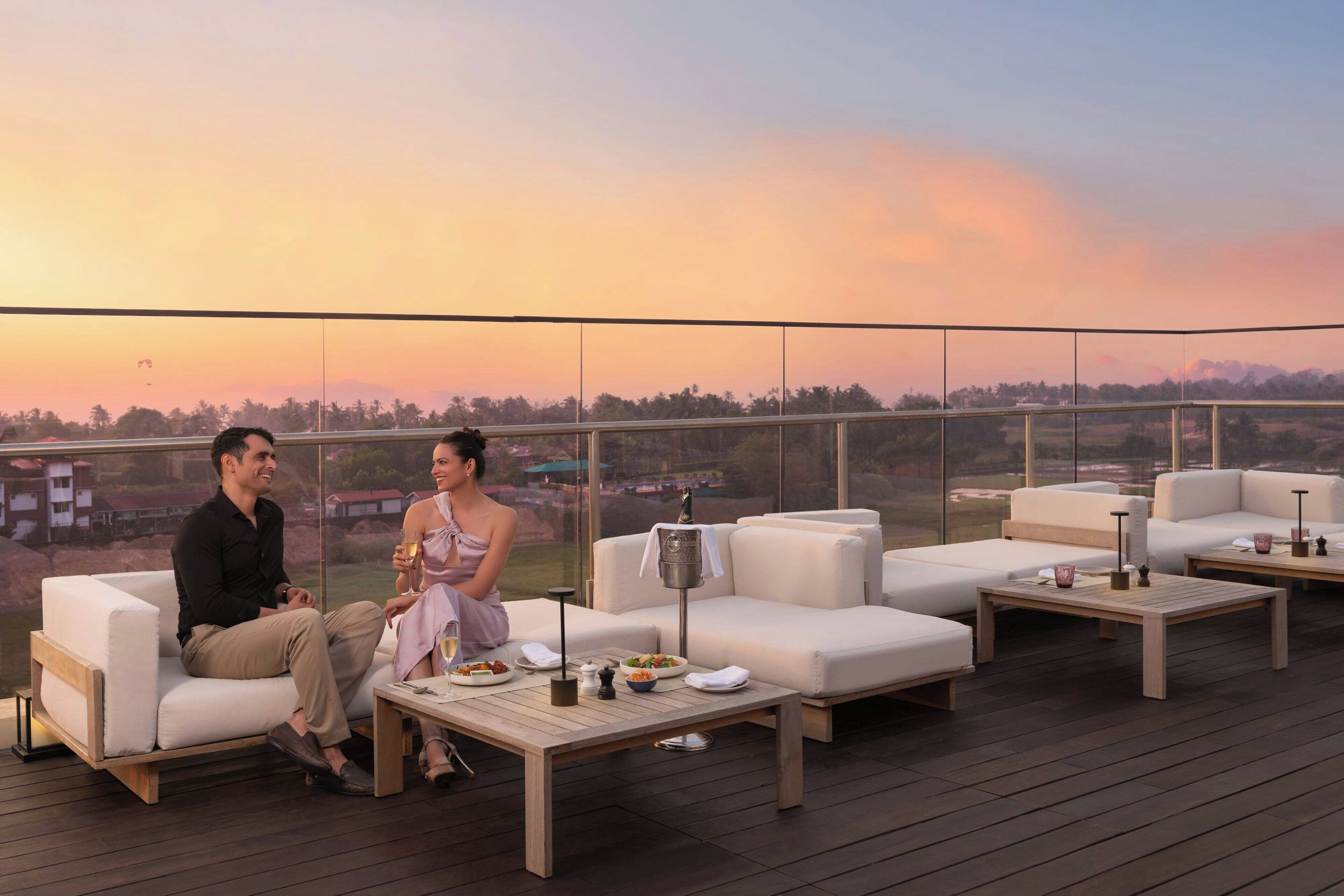 Una pareja sentada en una terraza con una vista panorámica del atardecer sobre un paisaje.
