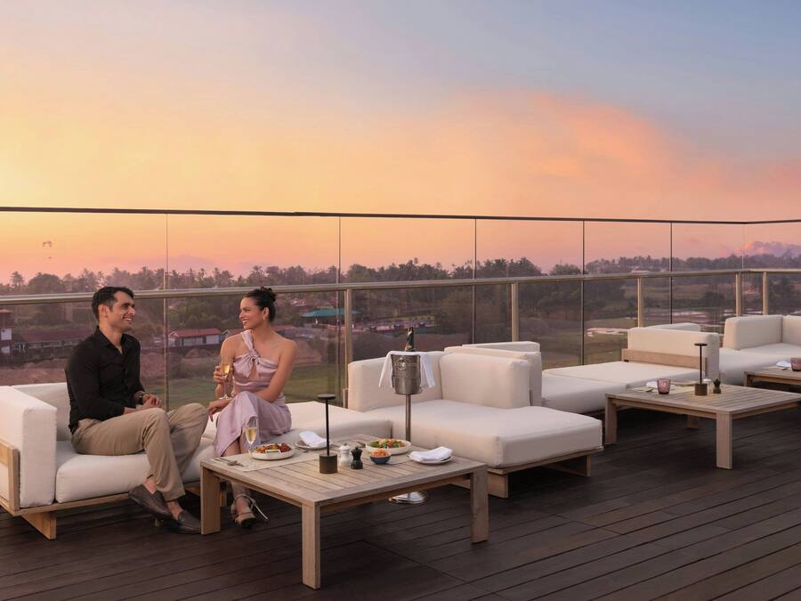 Una pareja sentada en una terraza con una vista panorámica del atardecer sobre un paisaje.
