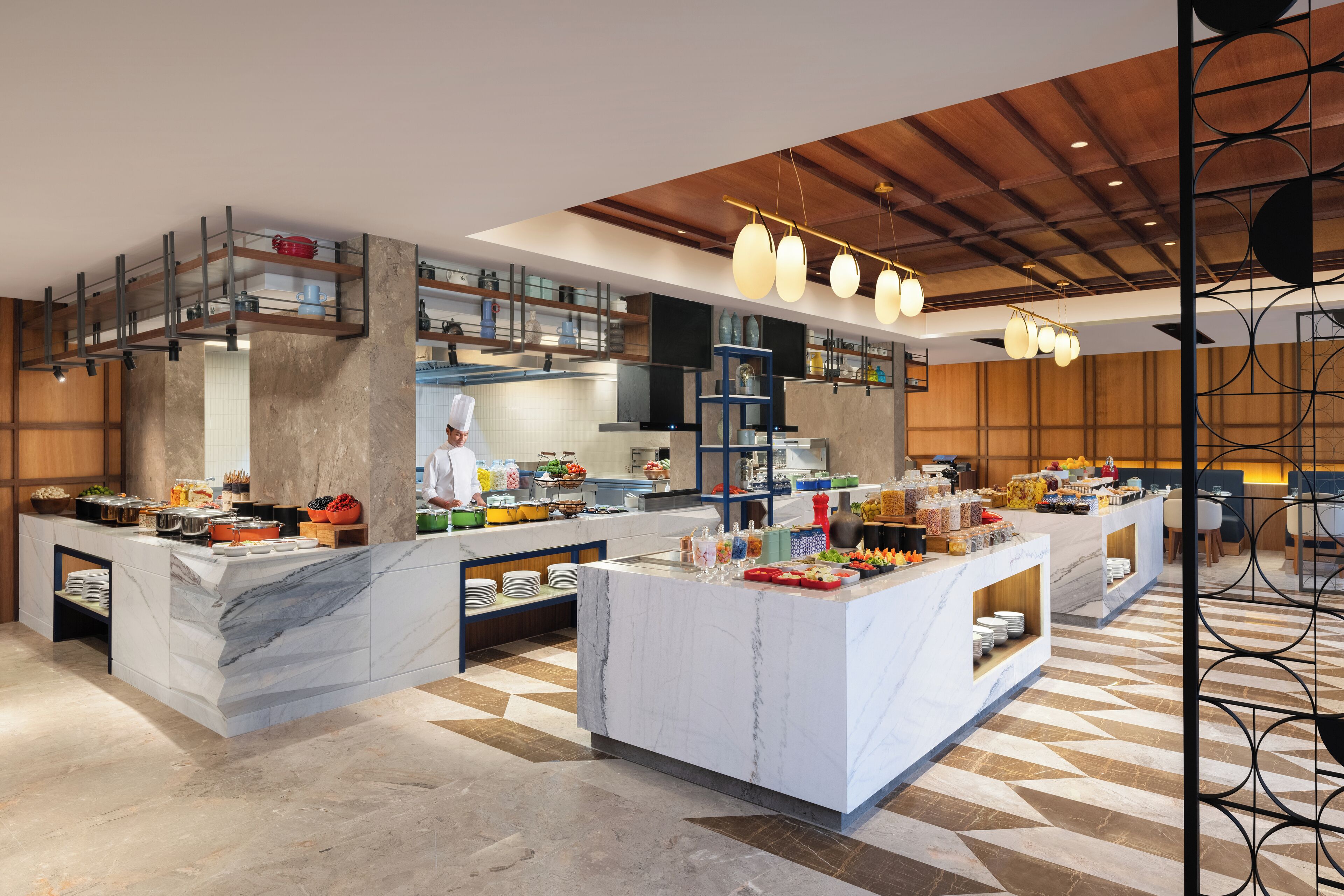 Een moderne keuken met marmeren aanrecht, een kok die bereidt en een buffet met diverse gerechten.
