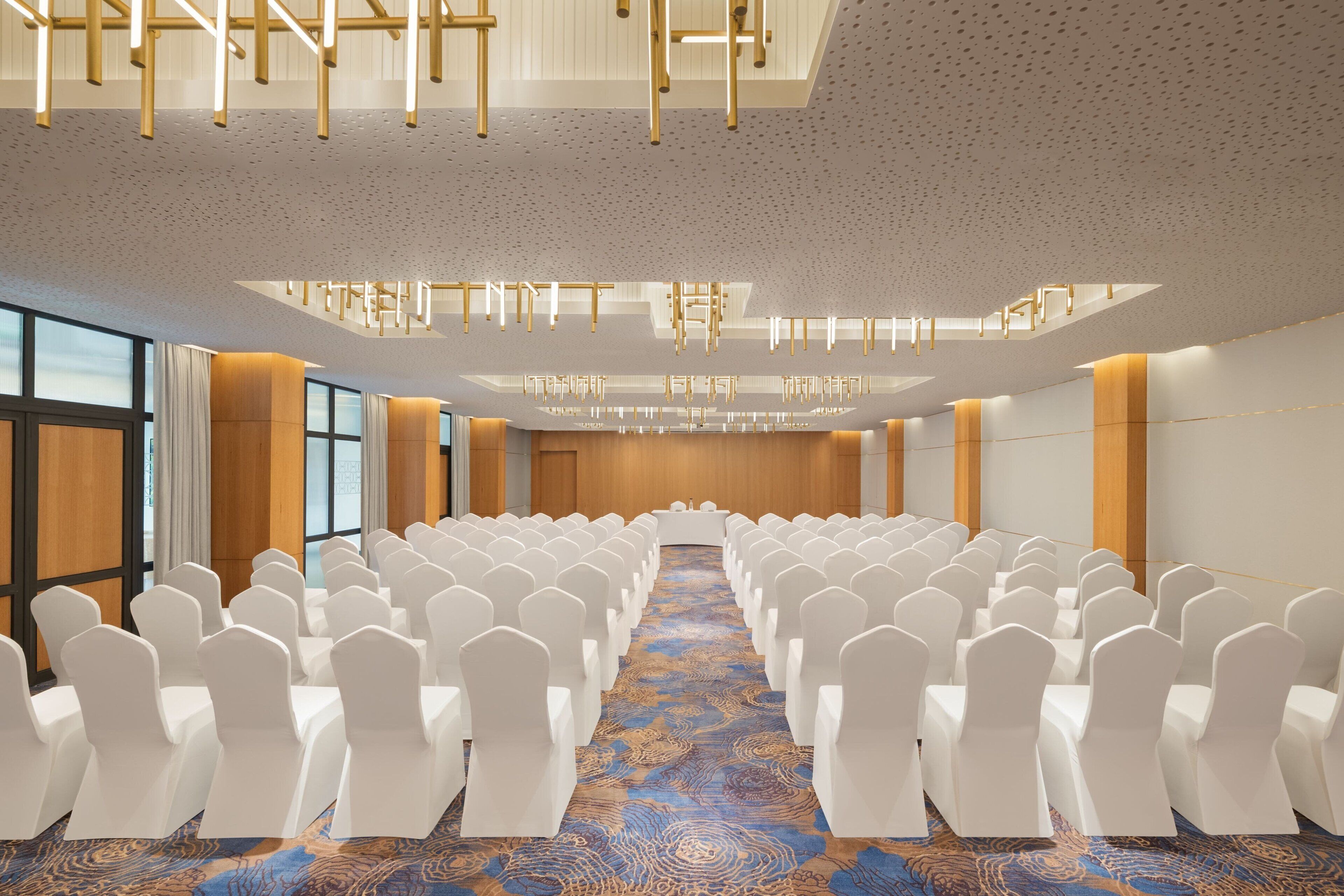 A conference room with rows of white chairs, a patterned carpet, and a modern ceiling design.
