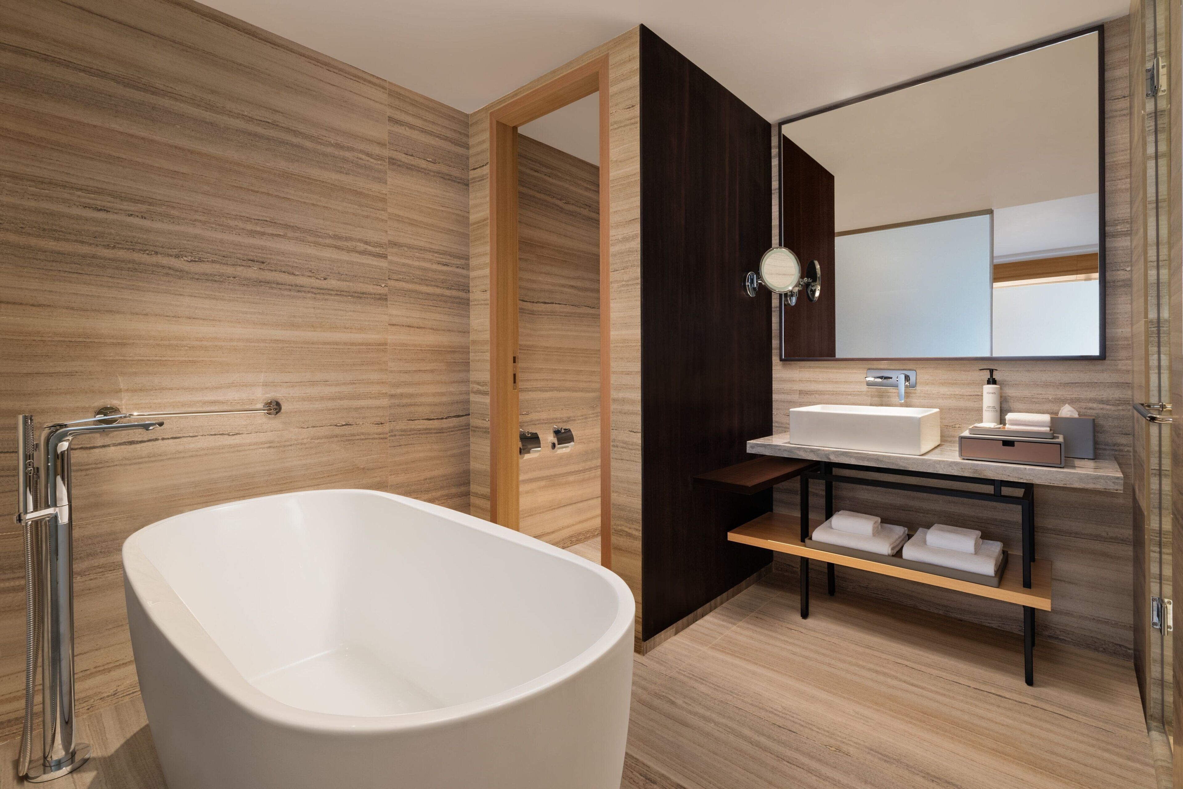 Een moderne badkamer met een vrijstaand bad, een wastafel met spiegel en een plank met handdoeken.