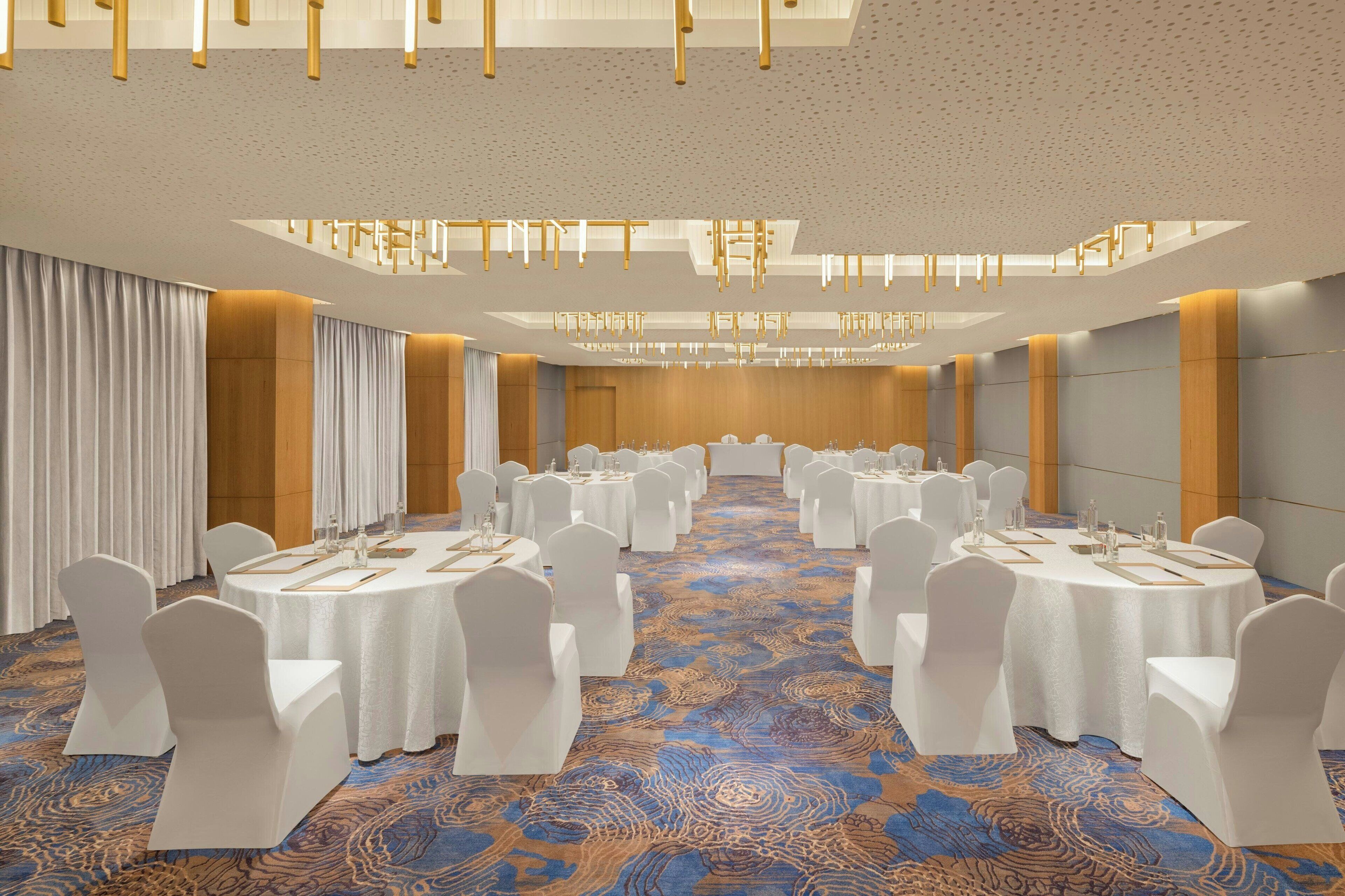 A conference room with round tables, white chairs, and a patterned carpet.
