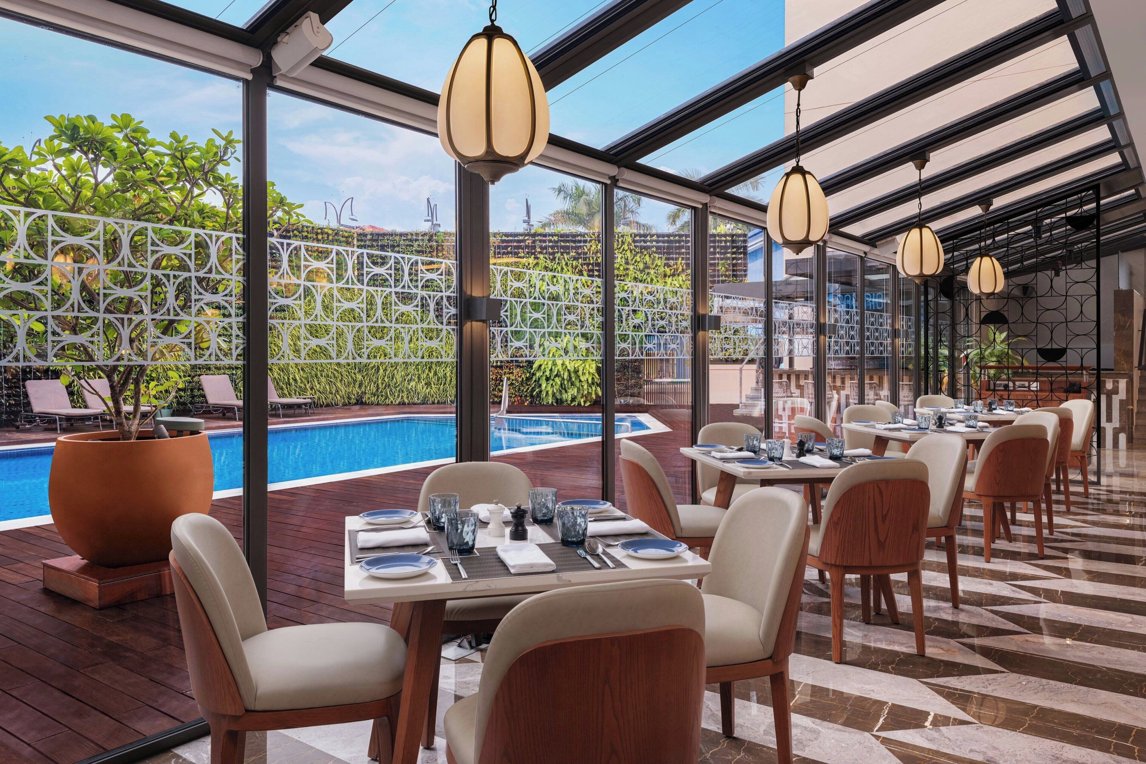 A restaurant with outdoor seating overlooking a pool, featuring modern furniture and pendant lighting.