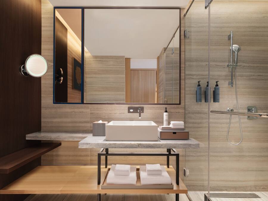 Un baño moderno con un espejo grande, un lavamanos, una ducha y un tocador de madera.