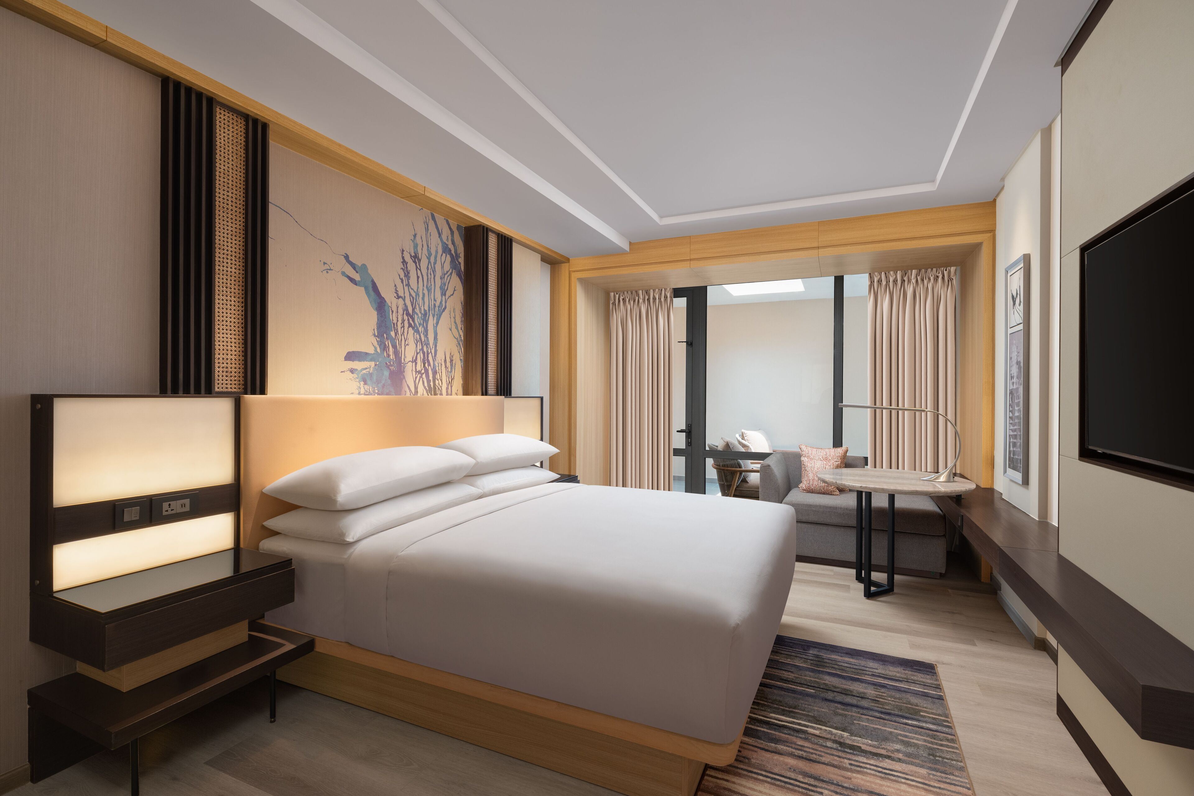 A modern hotel room with a large bed, bedside tables, a flat-screen TV, and a small seating area with a table and chairs.