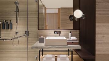 A modern bathroom with a large mirror, a built-in sink, a shower, and a vanity with toiletries.