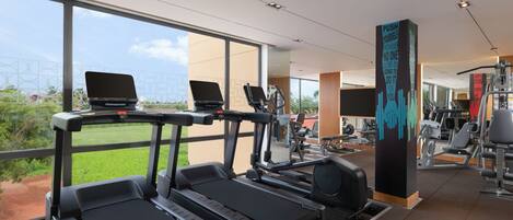Ein Fitnessstudio mit Laufbändern, einem Laptop auf einem davon und einem motivierenden Zitat an einer Säule.