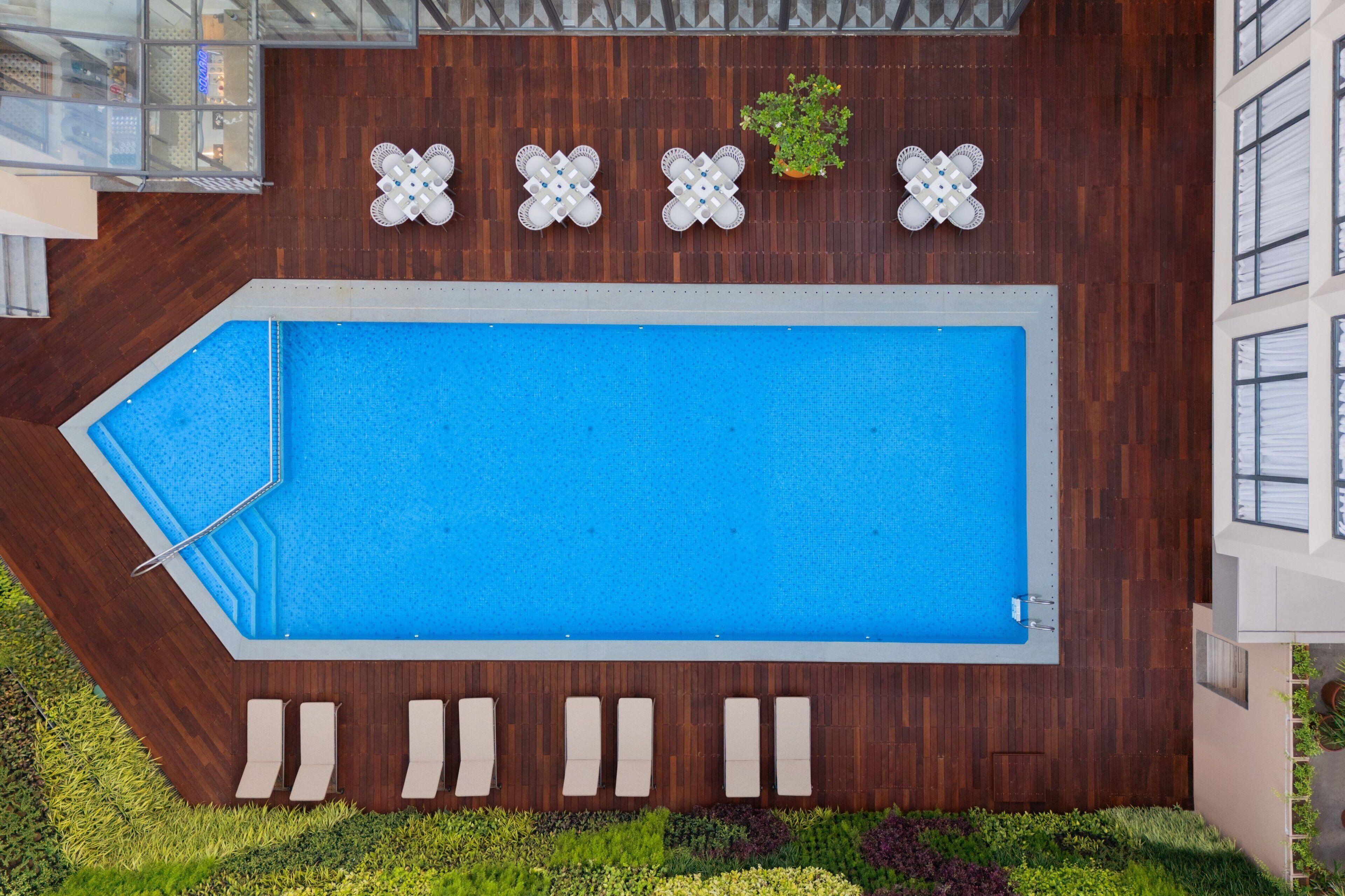Una piscina rectangular con un deck de madera alrededor, cuatro macetas blancas decorativas y una planta pequeña en maceta.