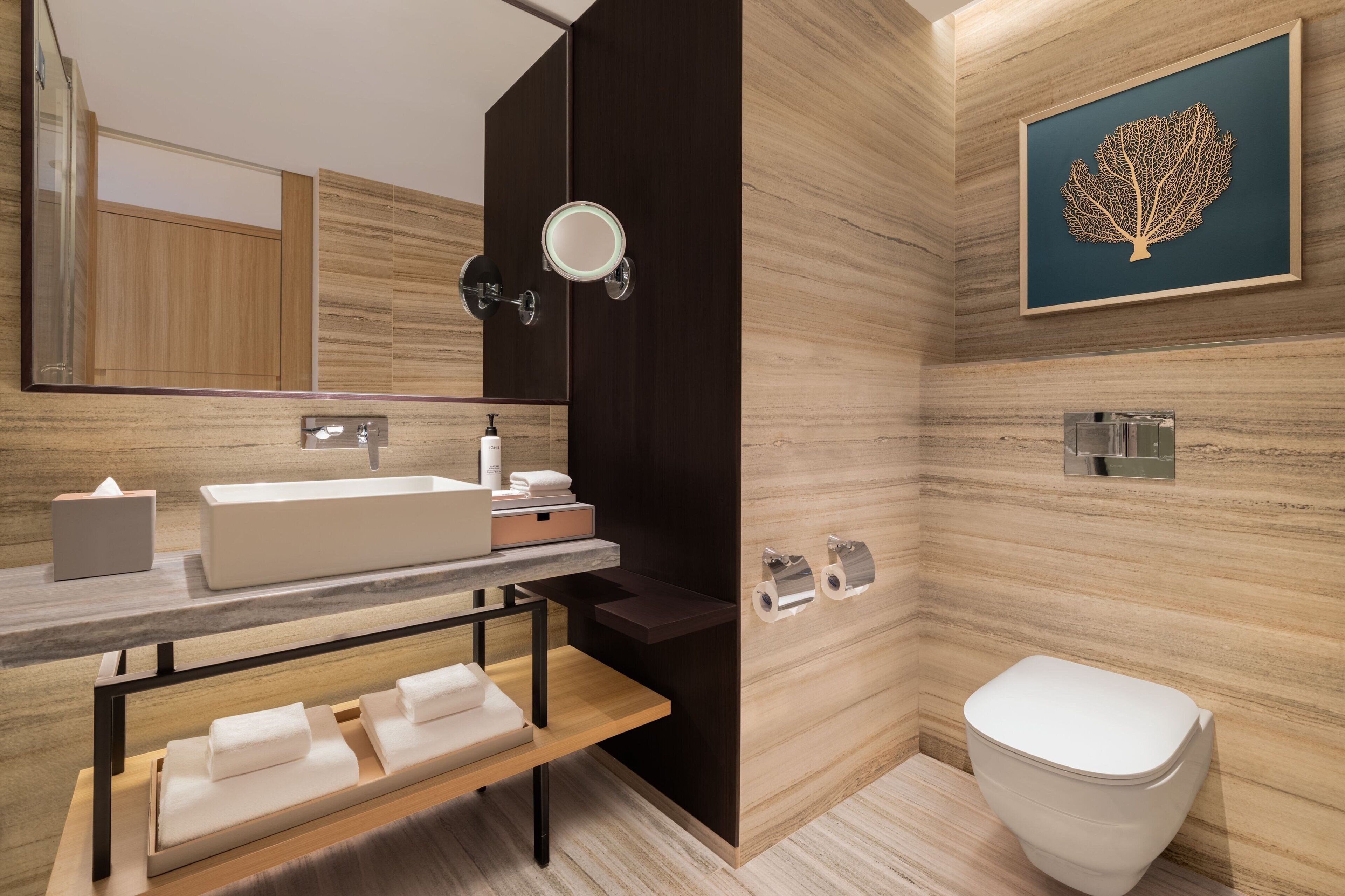 A modern bathroom with a large mirror, a sink, a toilet, and a bench.