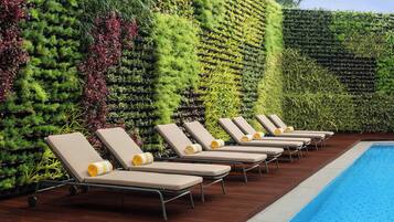Zona de piscina con sillones de descanso y un jardín vertical.