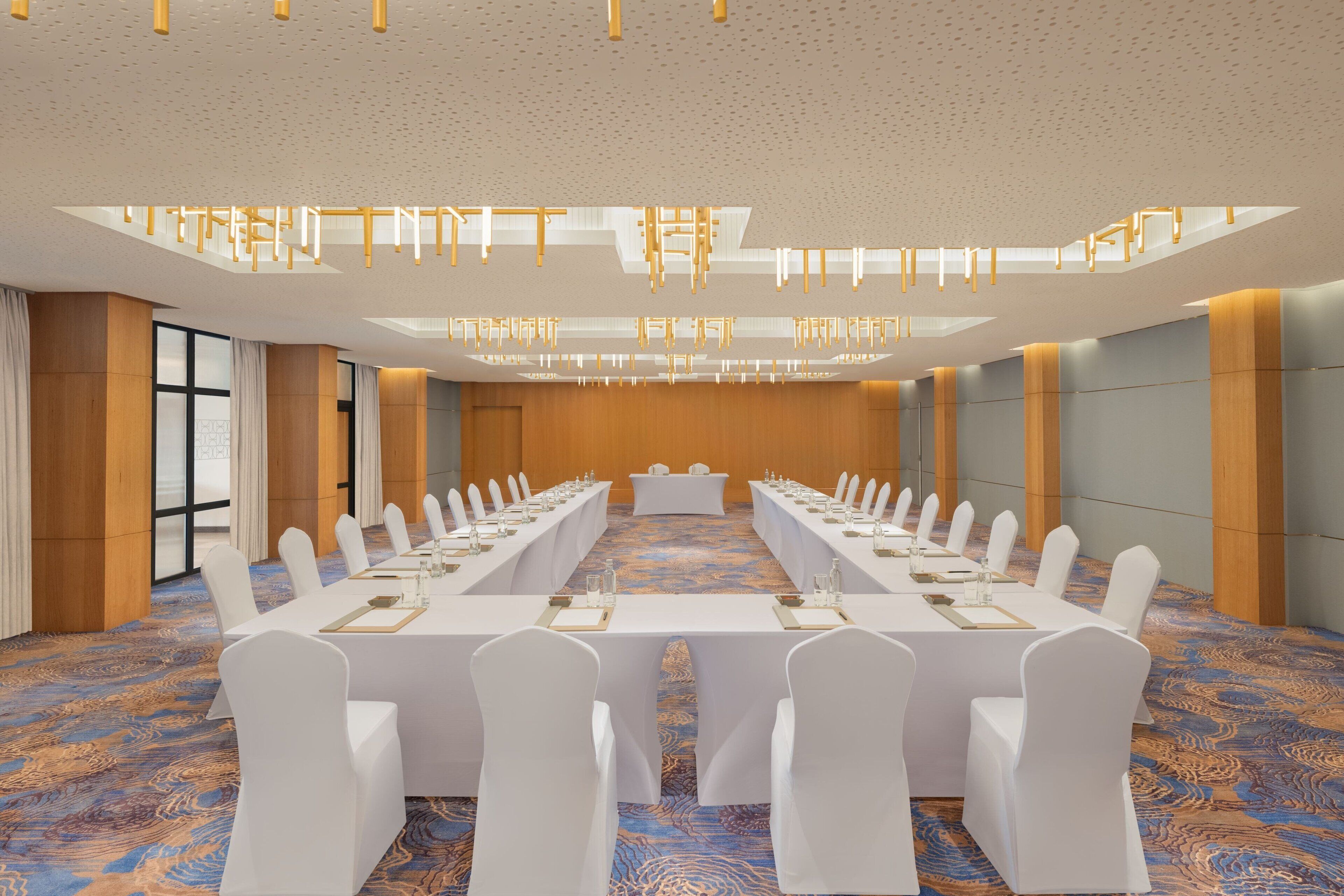 A conference room with a long table, white chairs, and a patterned carpet.