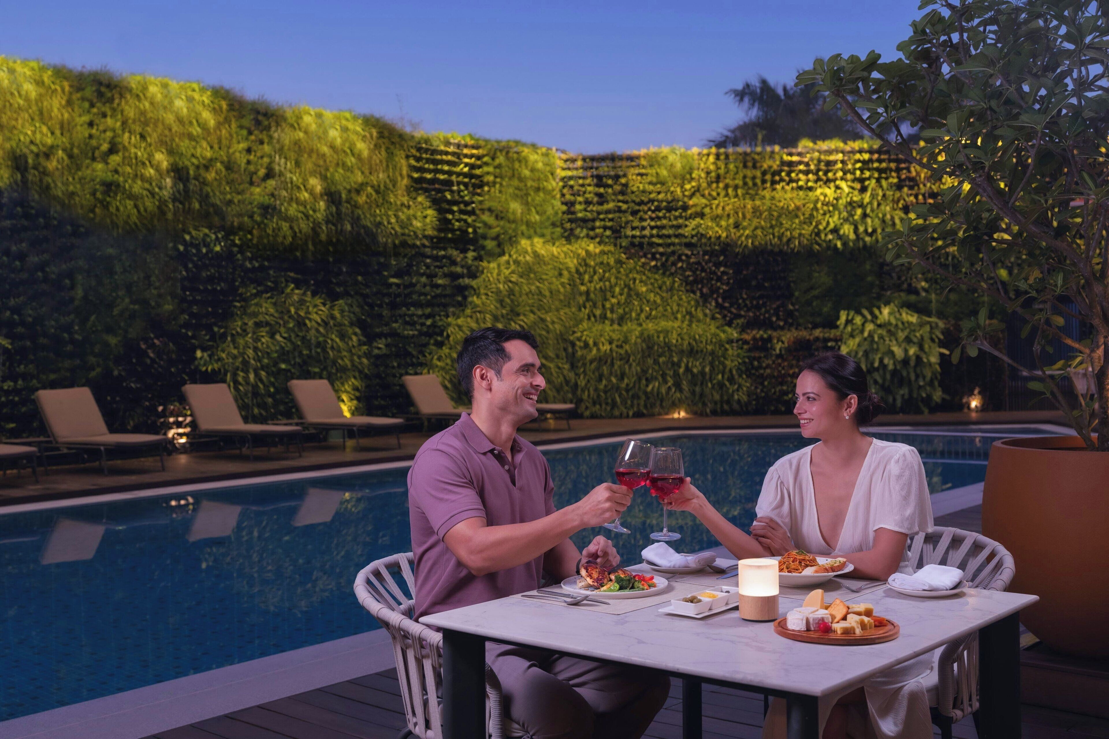 Una pareja cenando junto a una piscina con un exuberante telón de fondo verde.
