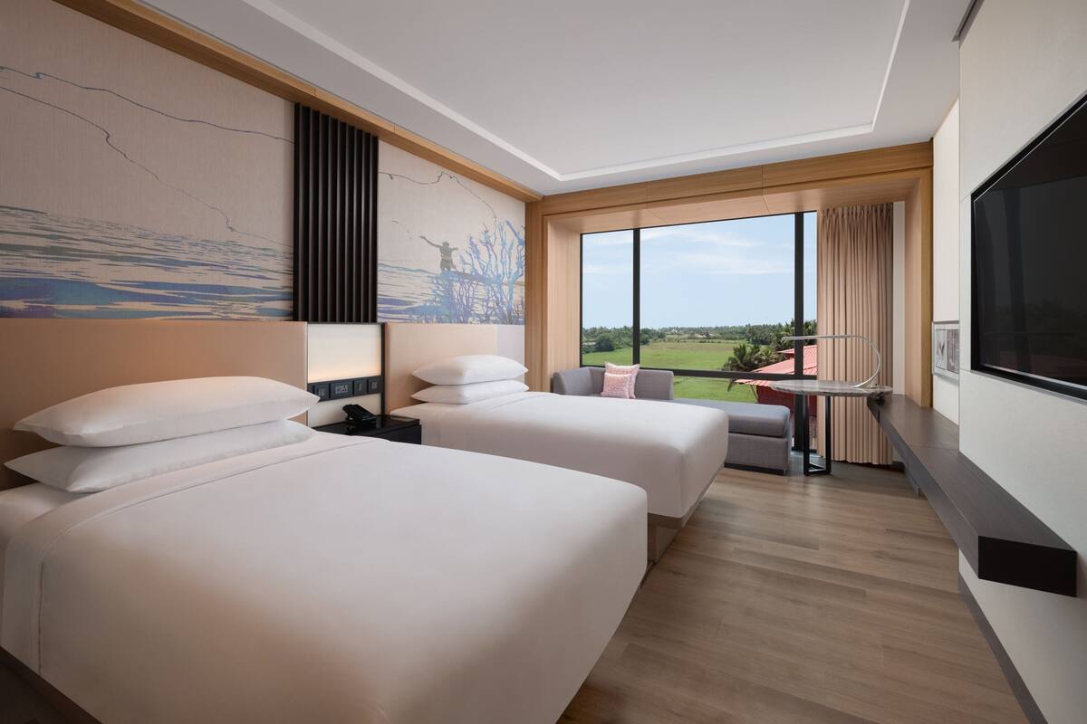 A hotel room with two beds, a TV, a balcony with a view, and a large window.