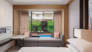 A modern hotel room with a sofa, a small table, a bed, and a view of a garden through a large window. - Courtyard By Marriott Goa Colva (Colva)