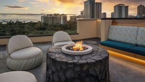 A rooftop terrace with a stone fire pit, seating area, and a view of the city skyline. - Marriott Vacation Club, Waikiki (Honolulu)