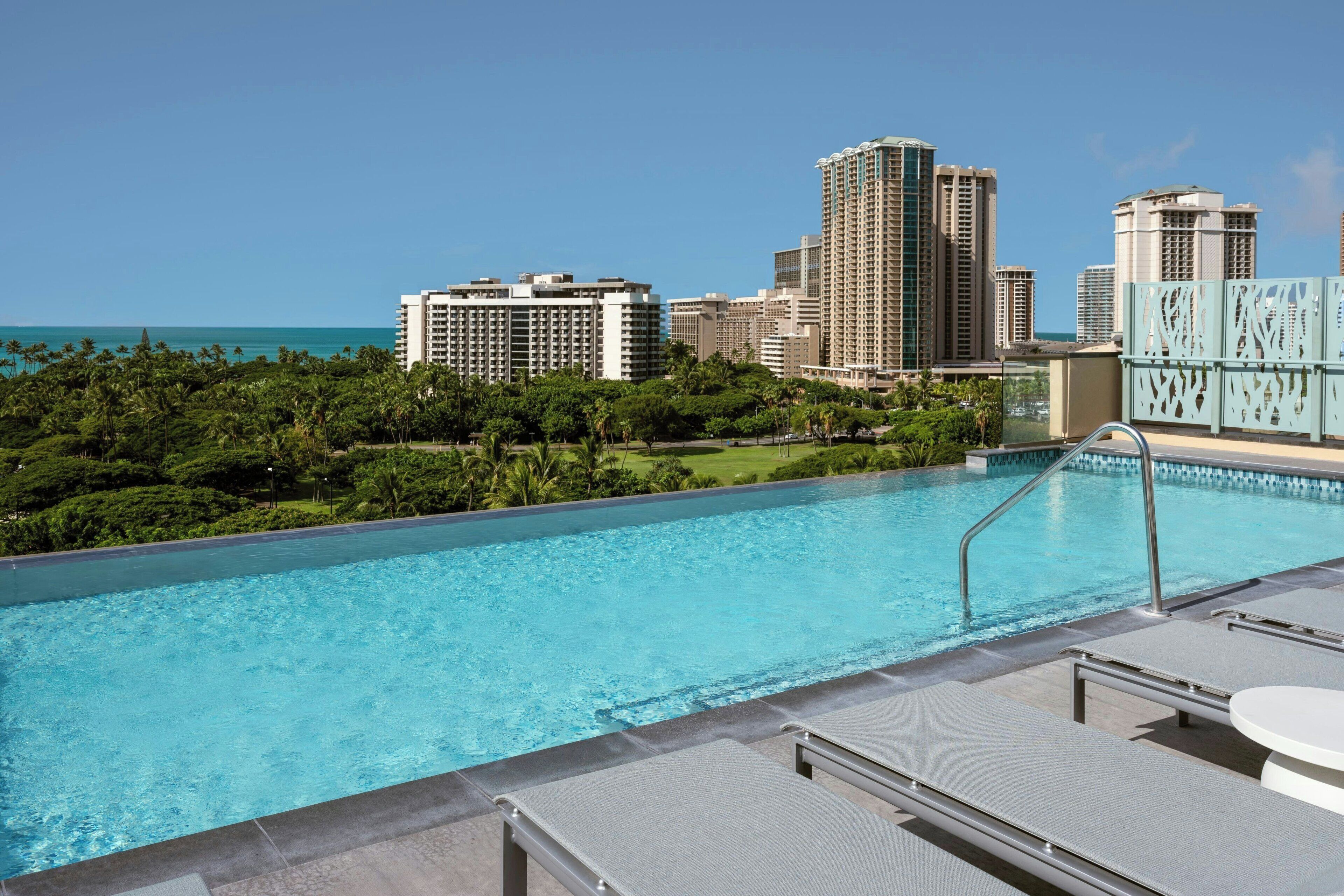 A swimming pool with a cityscape and palm trees in the background.