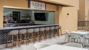 An outdoor bar area with a sign reading "MaloLo Rooftop Bar & Bites," featuring a counter with bar stools and a seating area with tables and chairs. - Marriott Vacation Club, Waikiki (Honolulu)