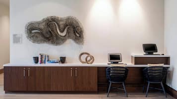 A modern kitchen with a wooden cabinet, a woven wall art piece, a flat-screen TV, and two black chairs.