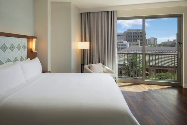 Habitación de hotel con una cama grande, una silla, vistas de la ciudad a través de un ventanal corredero y una pared con diseño.