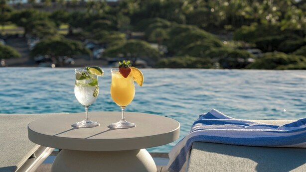 Two cocktails on a round table by a poolside with a view of palm trees and the ocean. - Marriott Vacation Club, Waikiki (Honolulu)