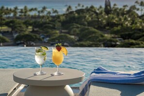 Two cocktails on a round table by a poolside with a view of palm trees and the ocean. - Marriott Vacation Club, Waikiki (Honolulu)
