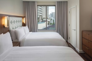 A hotel room with two beds, a view of the city, and a wooden dresser.