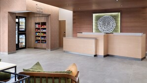 Un área de recepción con un mostrador de madera, un refrigerador lleno de bebidas y una zona de estar con un cojín verde.