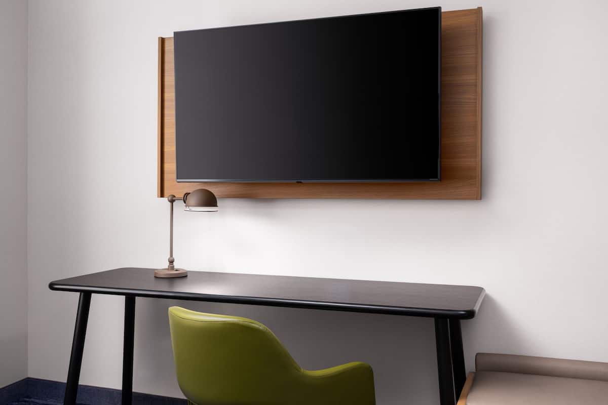 A modern room with a large flat-screen TV mounted on a wooden panel, a desk with a lamp, and a green chair.