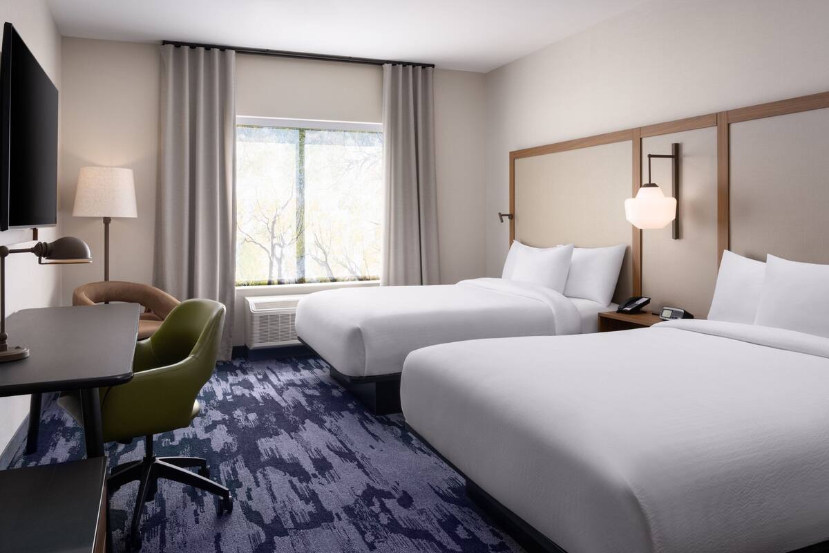 A hotel room with two beds, a desk, a chair, a TV, and a window with curtains.
